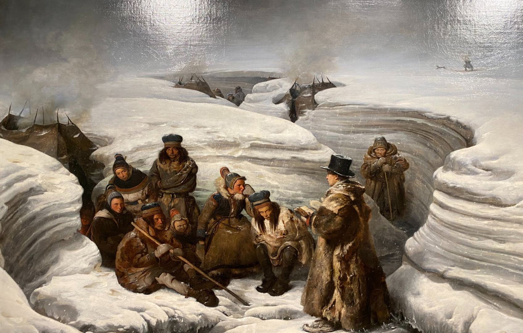 Bildet viser en gruppe mennesker som er samlet i et snødekket landskap. Bilder viser en person som står med ansiktet vendt mot gruppen og holder en bok foran seg - som om han forteller noe fra boken.